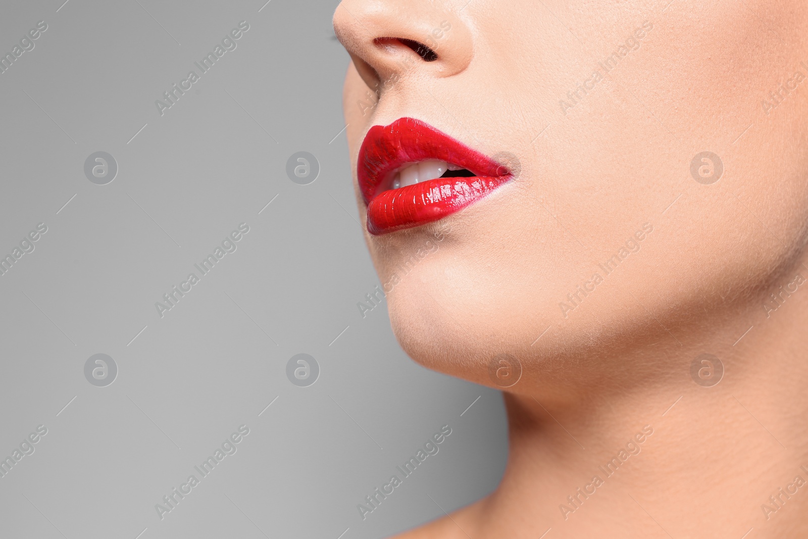 Photo of Beautiful young woman with red glossy lips on gray background, closeup. Space for text