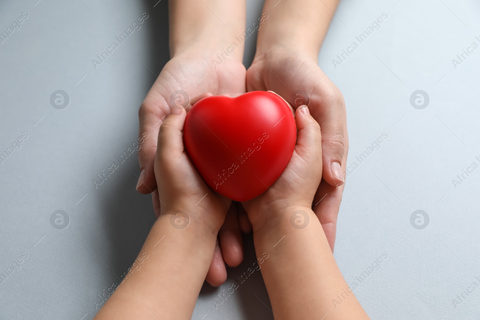 Photo of Mother and her child holding red decorative heart on gray background, top view