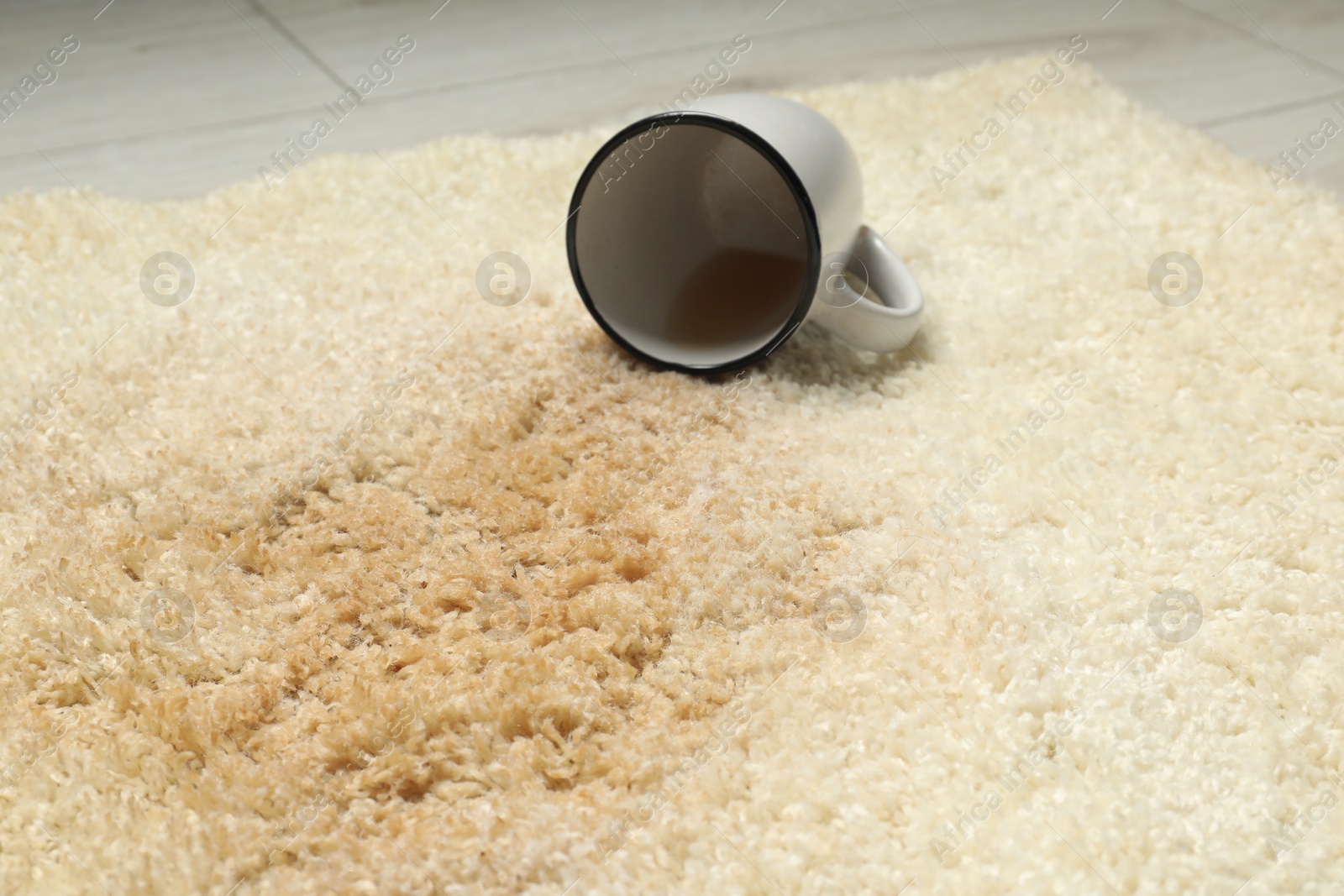 Photo of Overturned cup and spilled drink on beige carpet, closeup