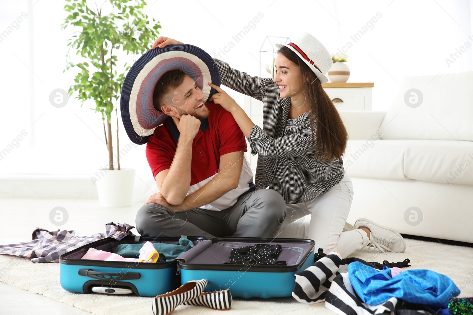 Photo of Young couple having fun while packing suitcase for summer journey at home