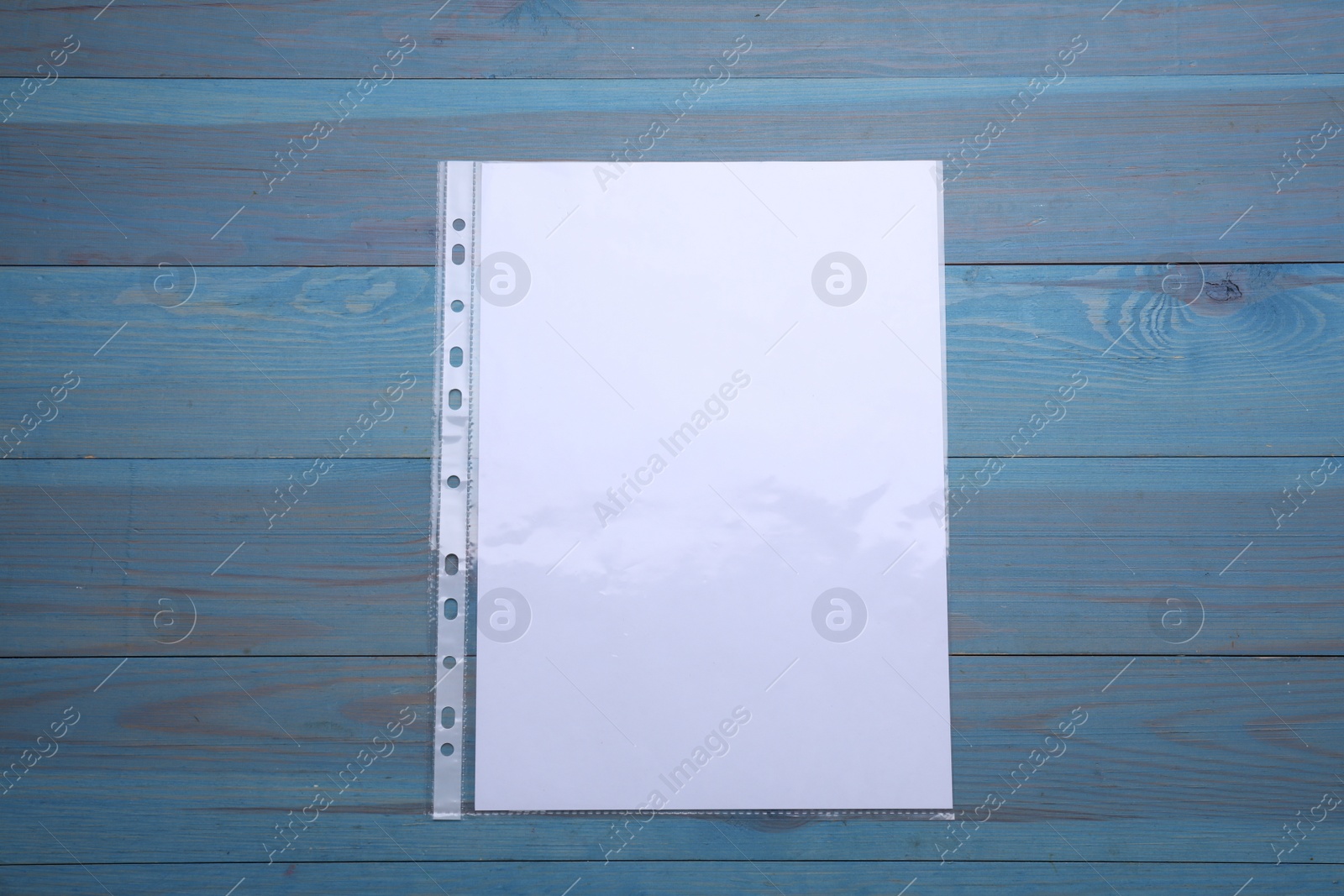 Photo of Punched pocket with paper sheet on light blue wooden table, top view