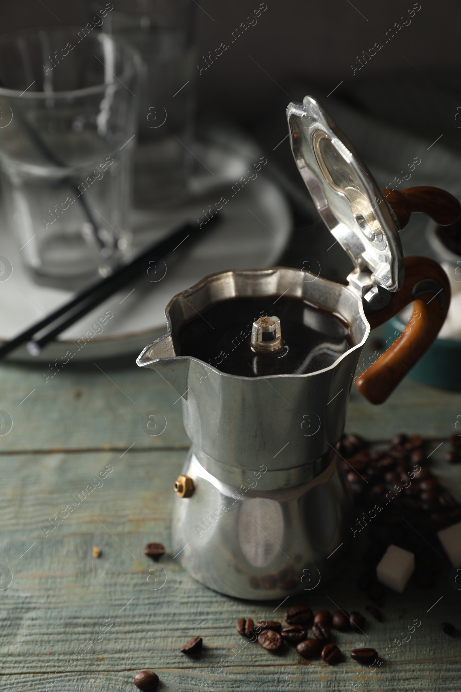 Photo of Brewed coffee in moka pot, beans and sugar cubes on rustic wooden table