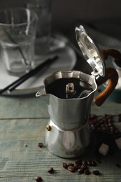Brewed coffee in moka pot, beans and sugar cubes on rustic wooden table