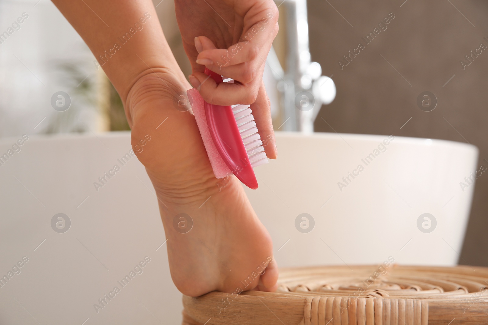 Photo of Woman using pumice stone for removing dead skin from feet in bathroom, closeup