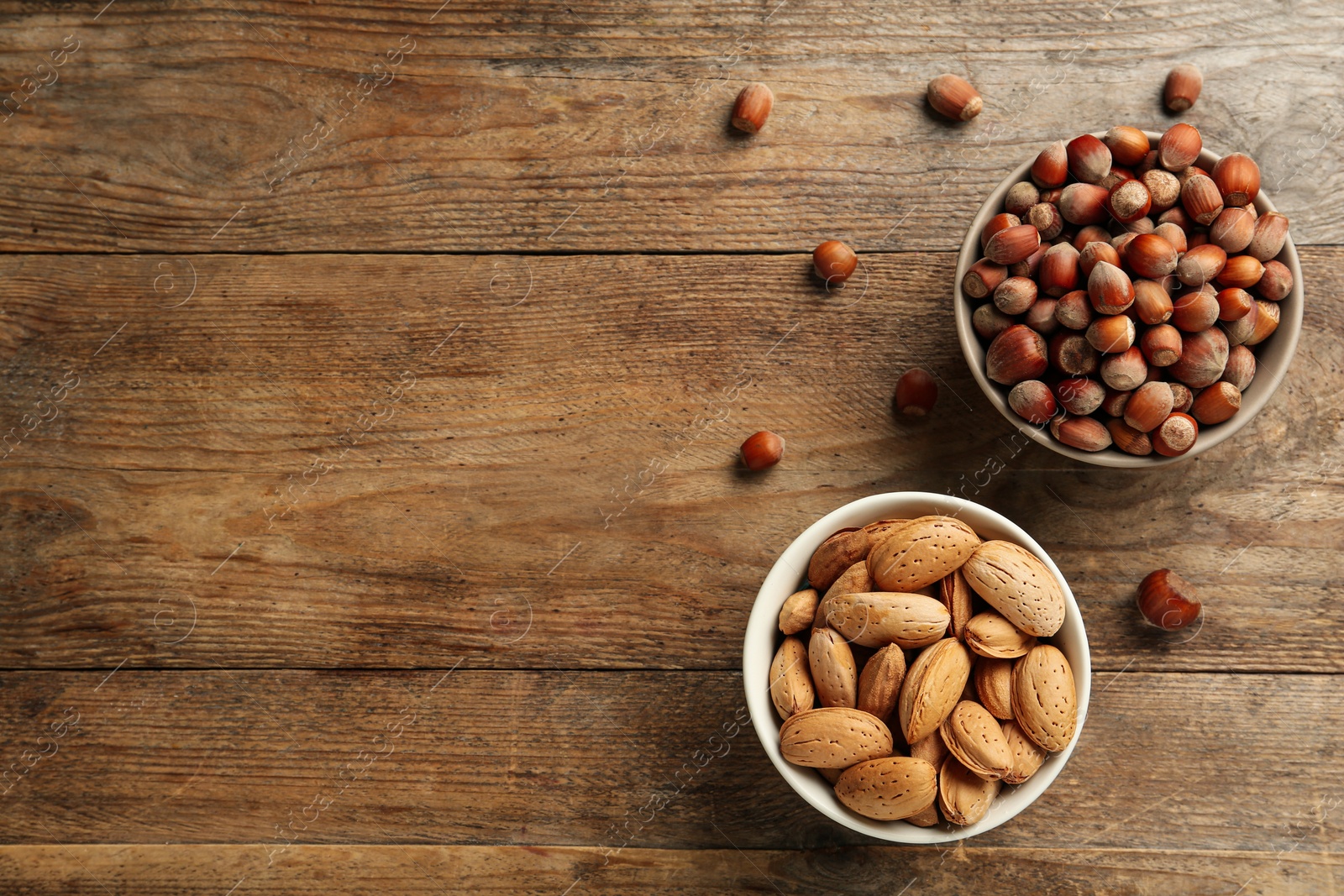 Photo of Ceramic bowls with nuts on wooden table, flat lay and space for text. Cooking utensil