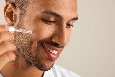 Photo of Handsome man applying cosmetic serum onto face on light grey background, closeup. Space for text