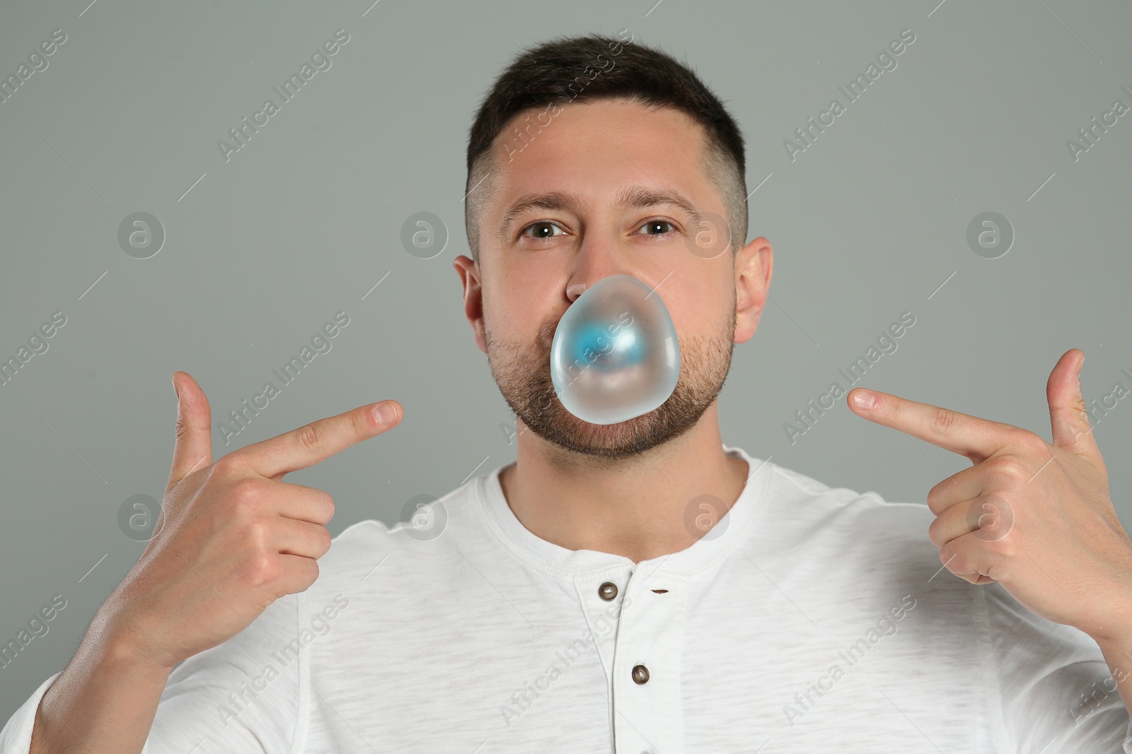 Photo of Handsome man blowing bubble gum on light grey background