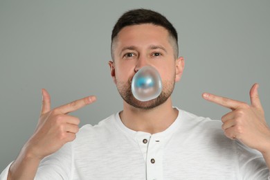 Handsome man blowing bubble gum on light grey background