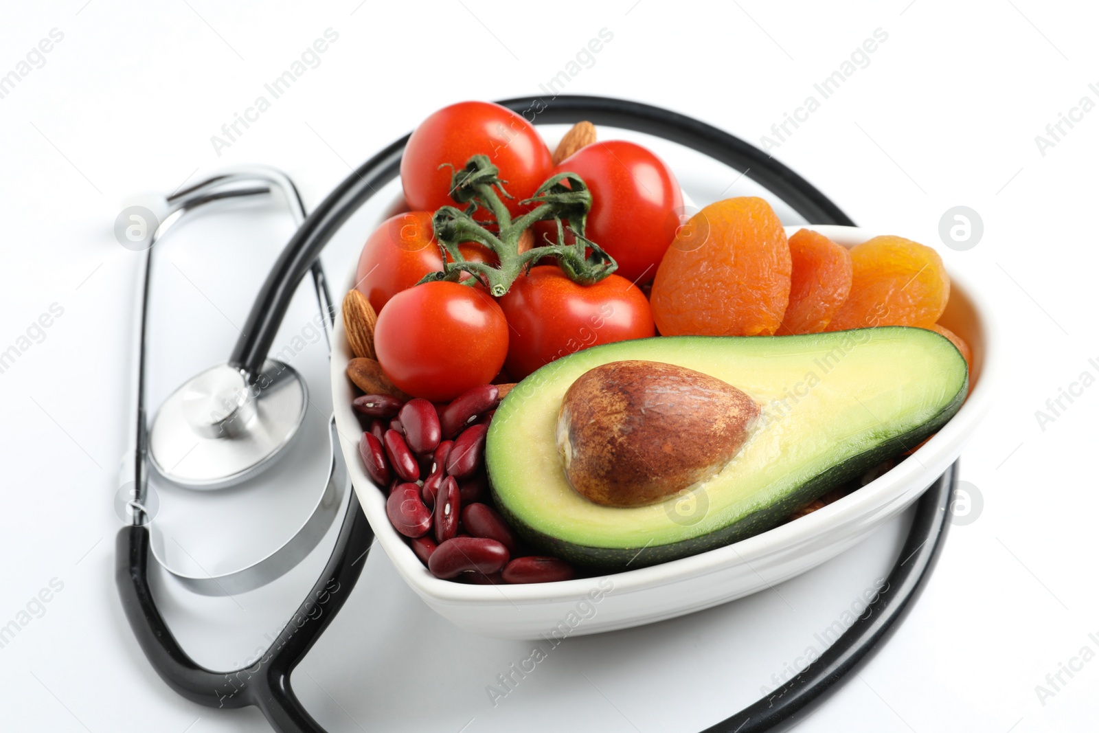 Photo of Heart shaped bowl with healthy products and stethoscope on white background