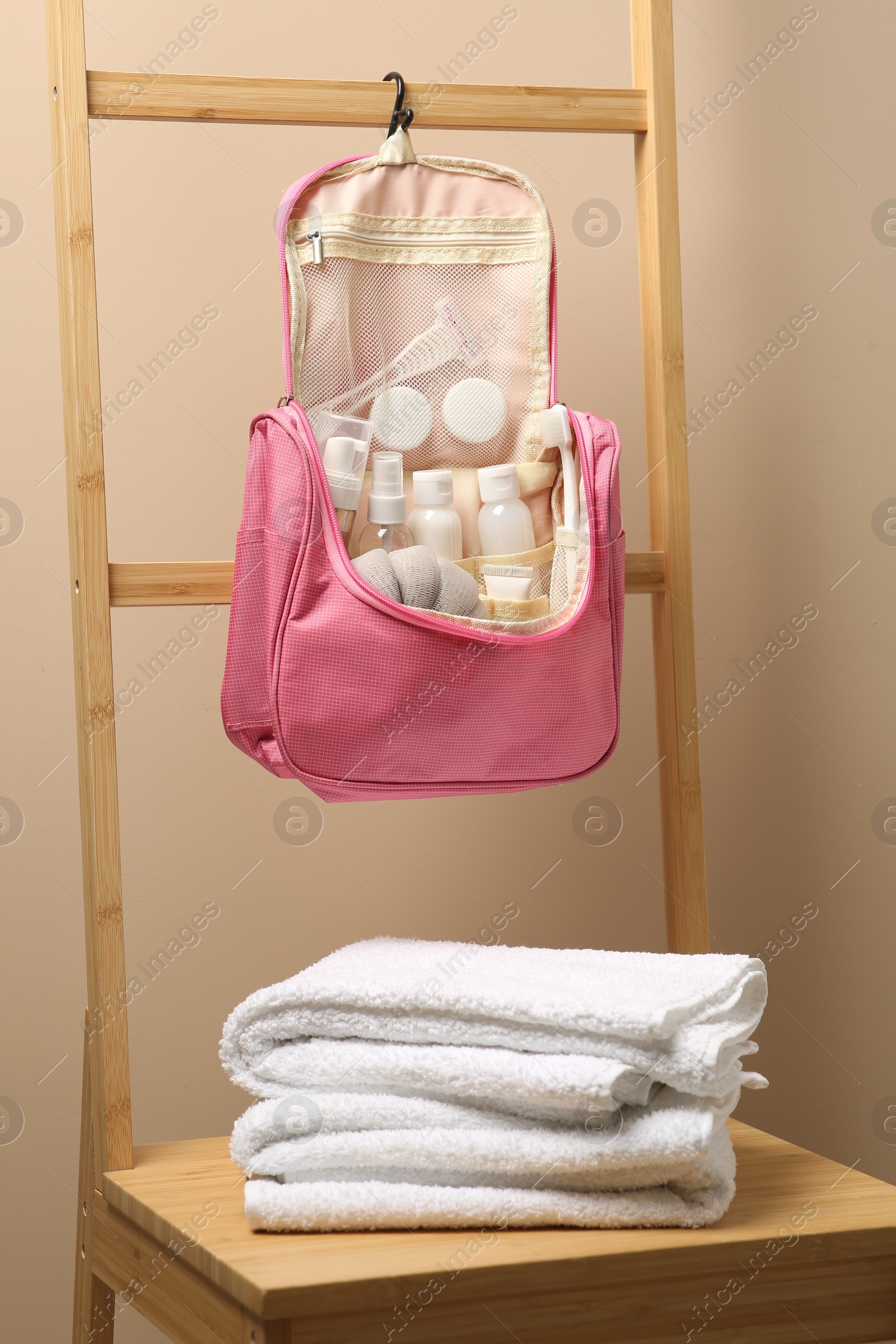 Photo of Cosmetic travel kit in compact toiletry bag and towels against beige wall. Bath accessories