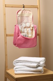 Cosmetic travel kit in compact toiletry bag and towels against beige wall. Bath accessories