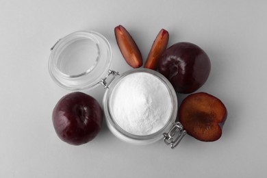 Photo of Jar with sweet fructose powder and ripe plums on white background, top view