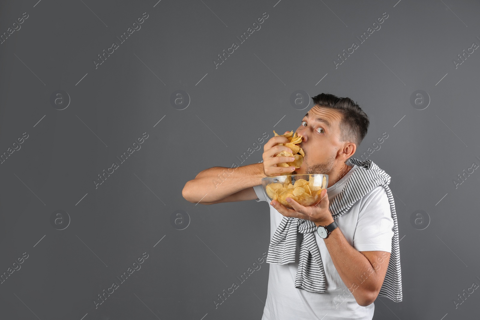 Photo of Man eating potato chips on grey background. Space for text