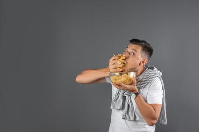 Man eating potato chips on grey background. Space for text