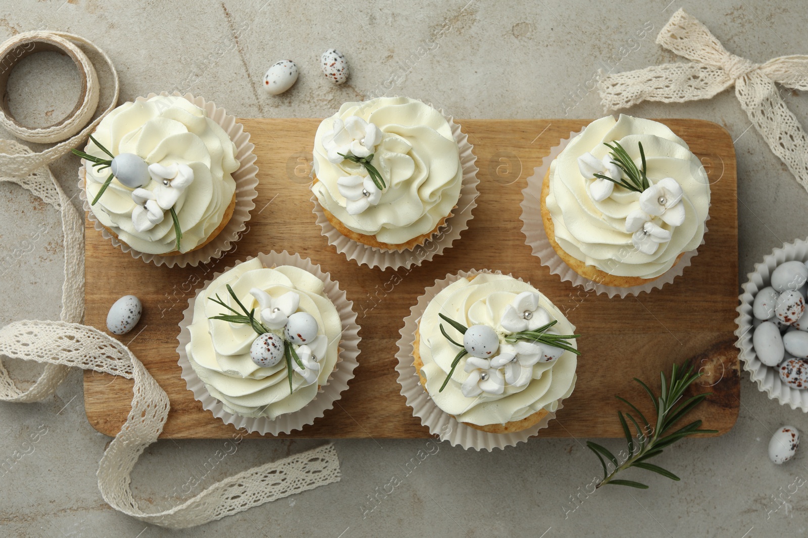 Photo of Tasty Easter cupcakes with vanilla cream, candies and ribbon on gray table, flat lay