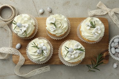 Tasty Easter cupcakes with vanilla cream, candies and ribbon on gray table, flat lay