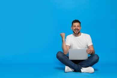 Happy man sitting with laptop on light blue background. Space for text