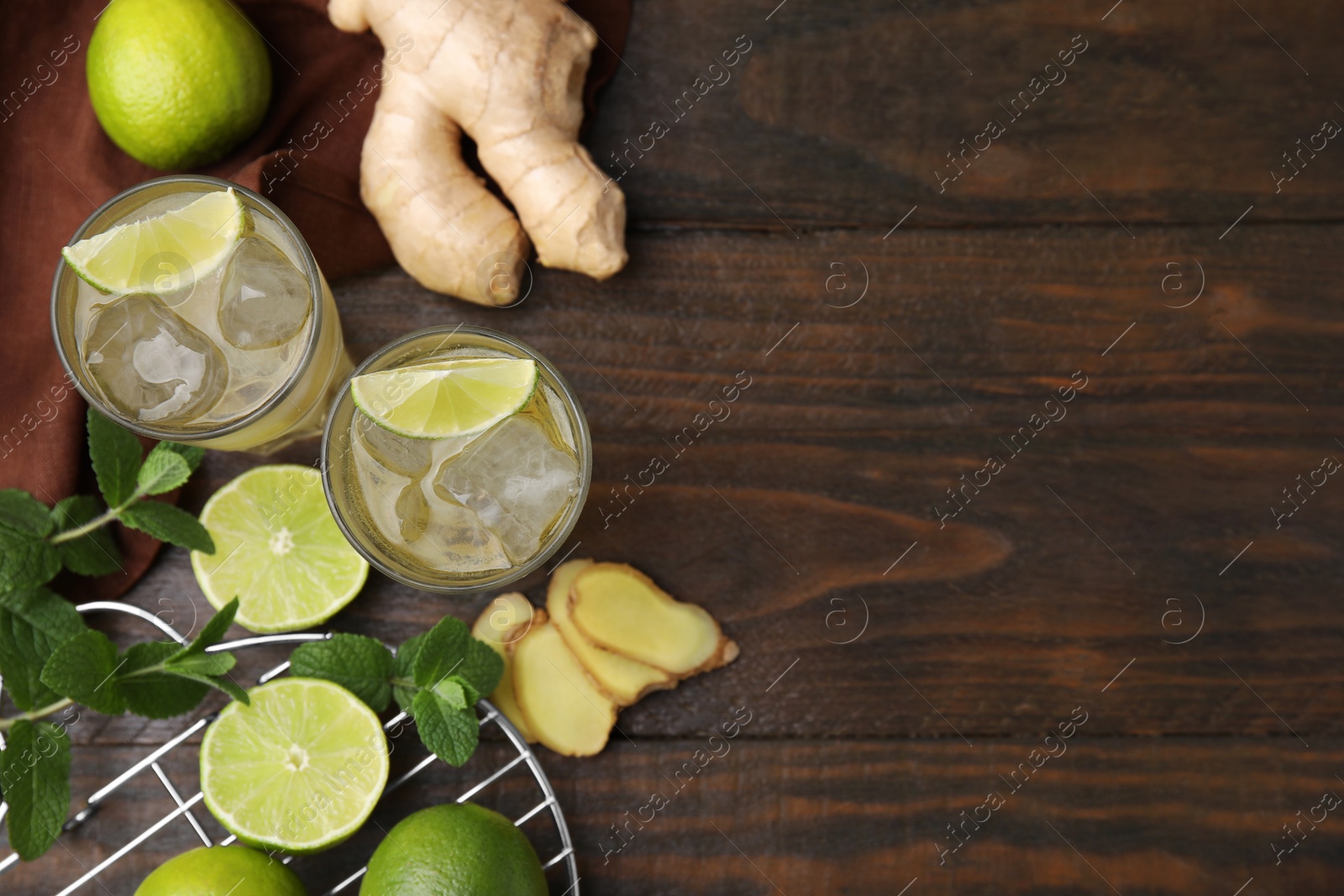 Photo of Glasses of tasty ginger ale with ice cubes and ingredients on wooden table, flat lay. Space for text