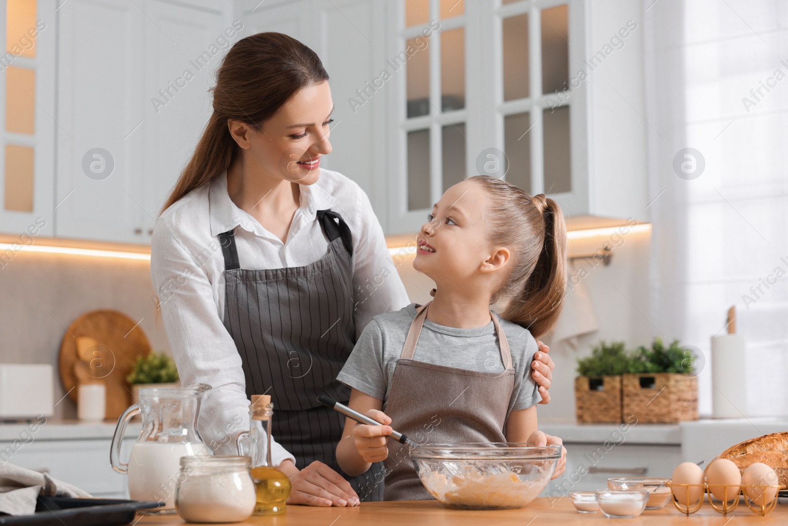 Photo of Making bread. Mother and her daughter preparing dough at wooden table in kitchen