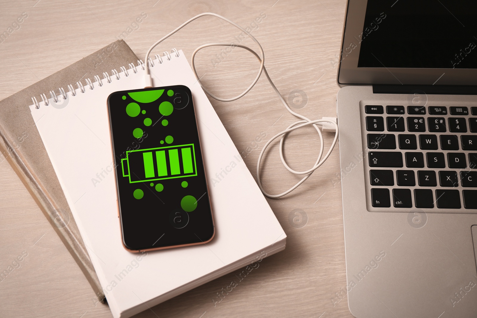 Image of Smartphone connected with charge cable to laptop on wooden table, above view