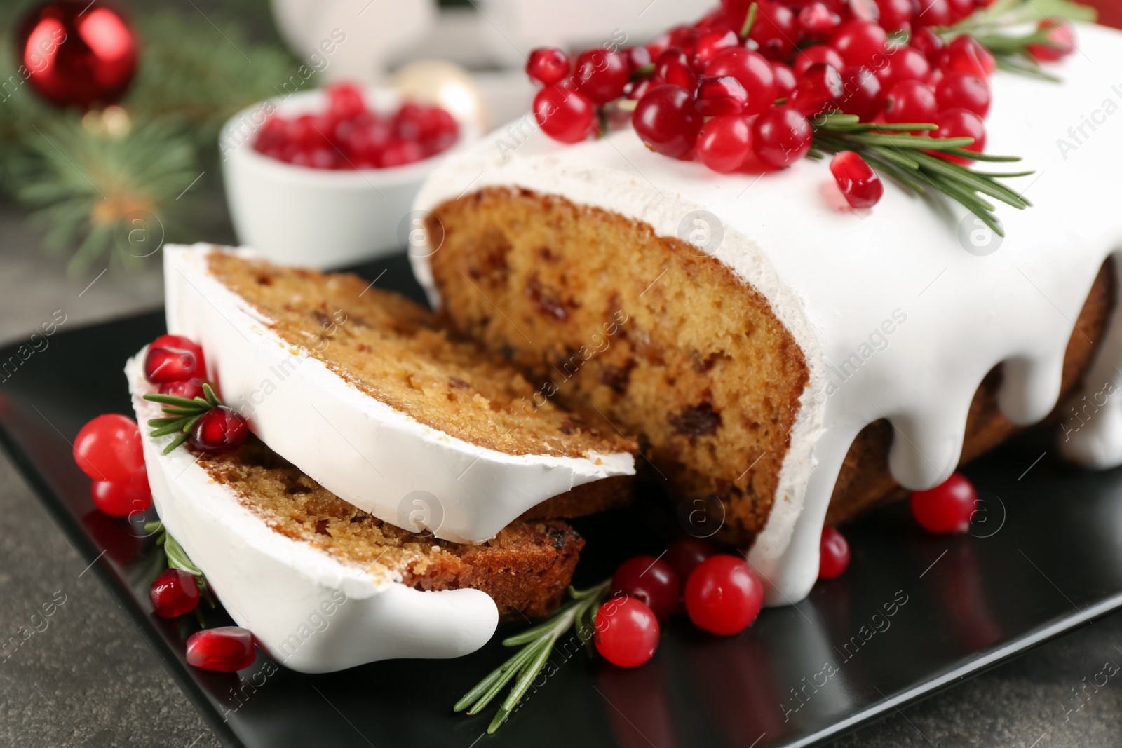Photo of Traditional classic Christmas cake decorated with cranberries, pomegranate seeds and rosemary on black plate, closeup