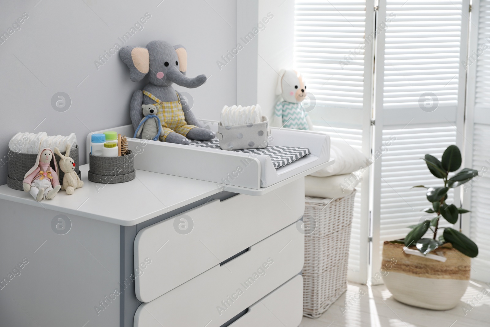 Photo of Chest of drawers with changing pad and tray in nursery. Baby room interior design