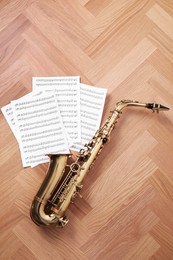 Beautiful saxophone and note sheets on wooden background, flat lay