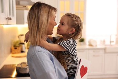 Photo of Little daughter congratulating her mom with greeting card in kitchen. Happy Mother's Day
