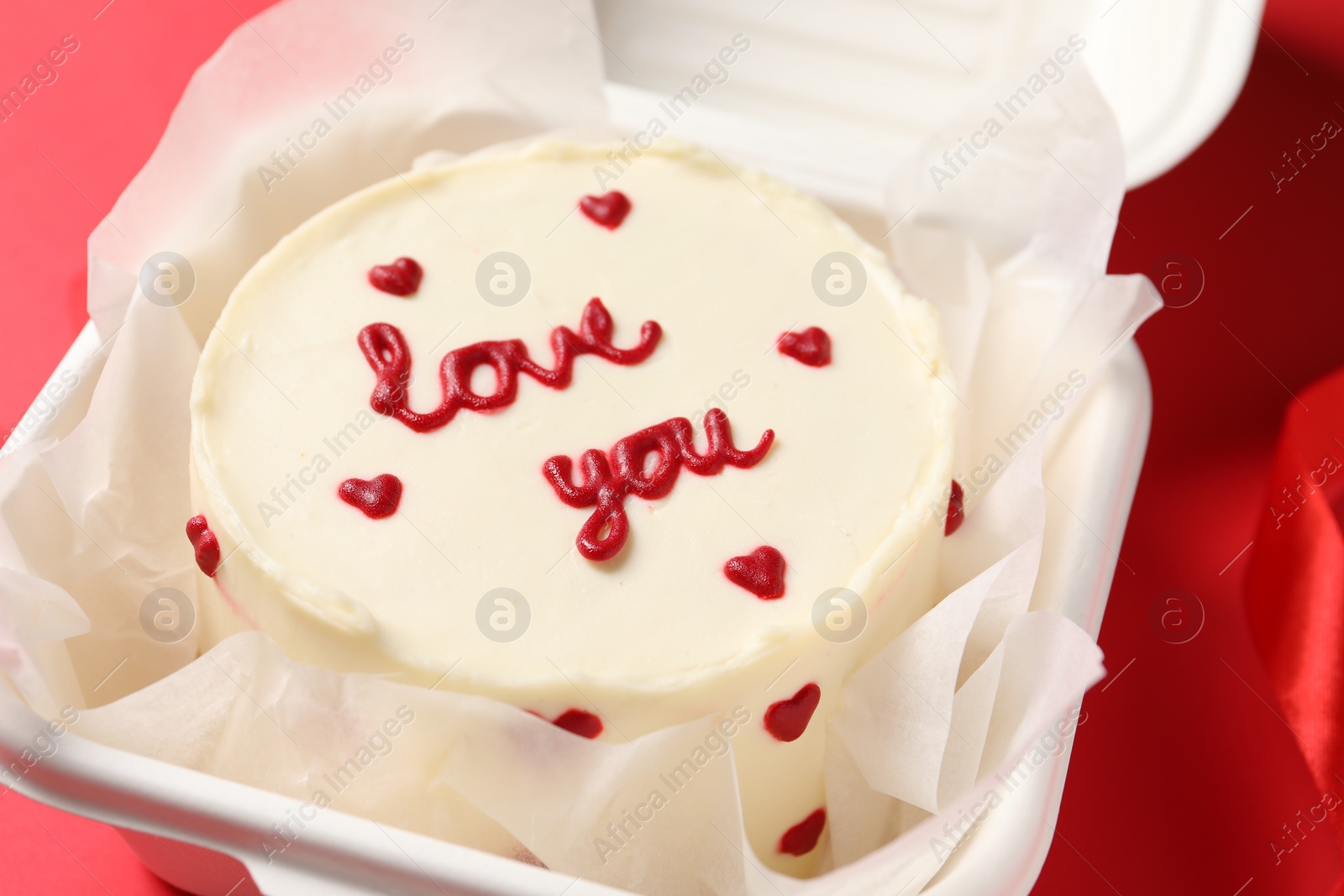 Photo of Bento cake with Love You text in takeaway box on red table, closeup. St. Valentine's day surprise