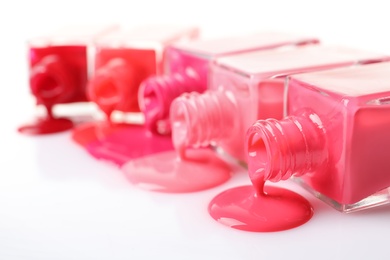 Spilled different nail polishes with bottles on white background, closeup