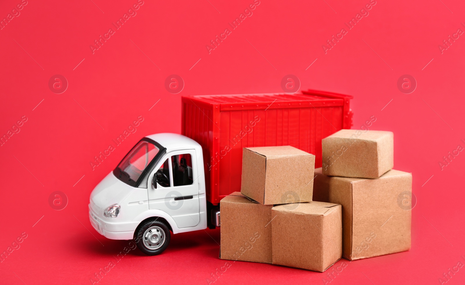 Photo of Truck model and carton boxes on red background. Courier service