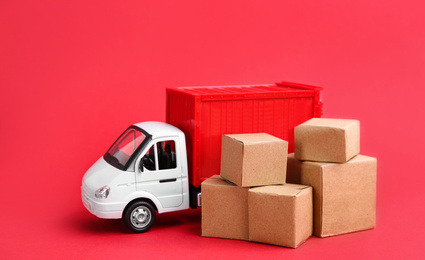 Photo of Truck model and carton boxes on red background. Courier service