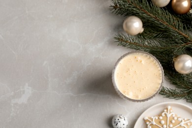 Photo of Glass of delicious eggnog and decorated fir branch on light marble table, flat lay. Space for text