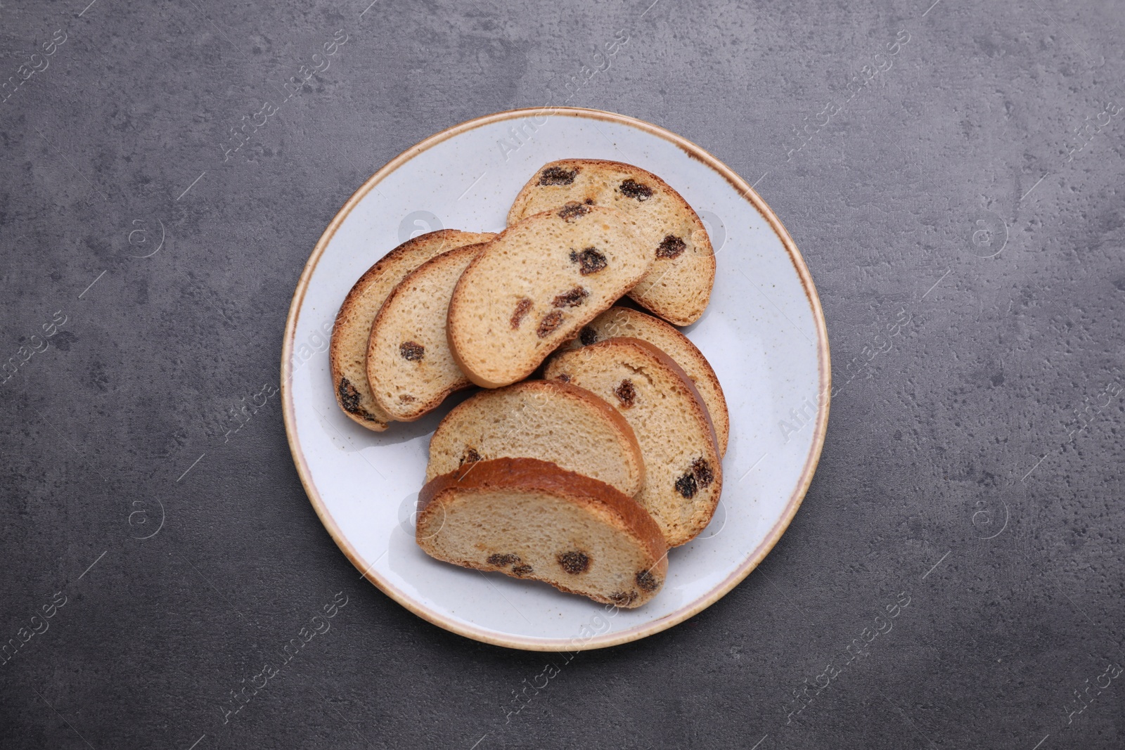 Photo of Plate of sweet hard chuck crackers with raisins on grey table, top view