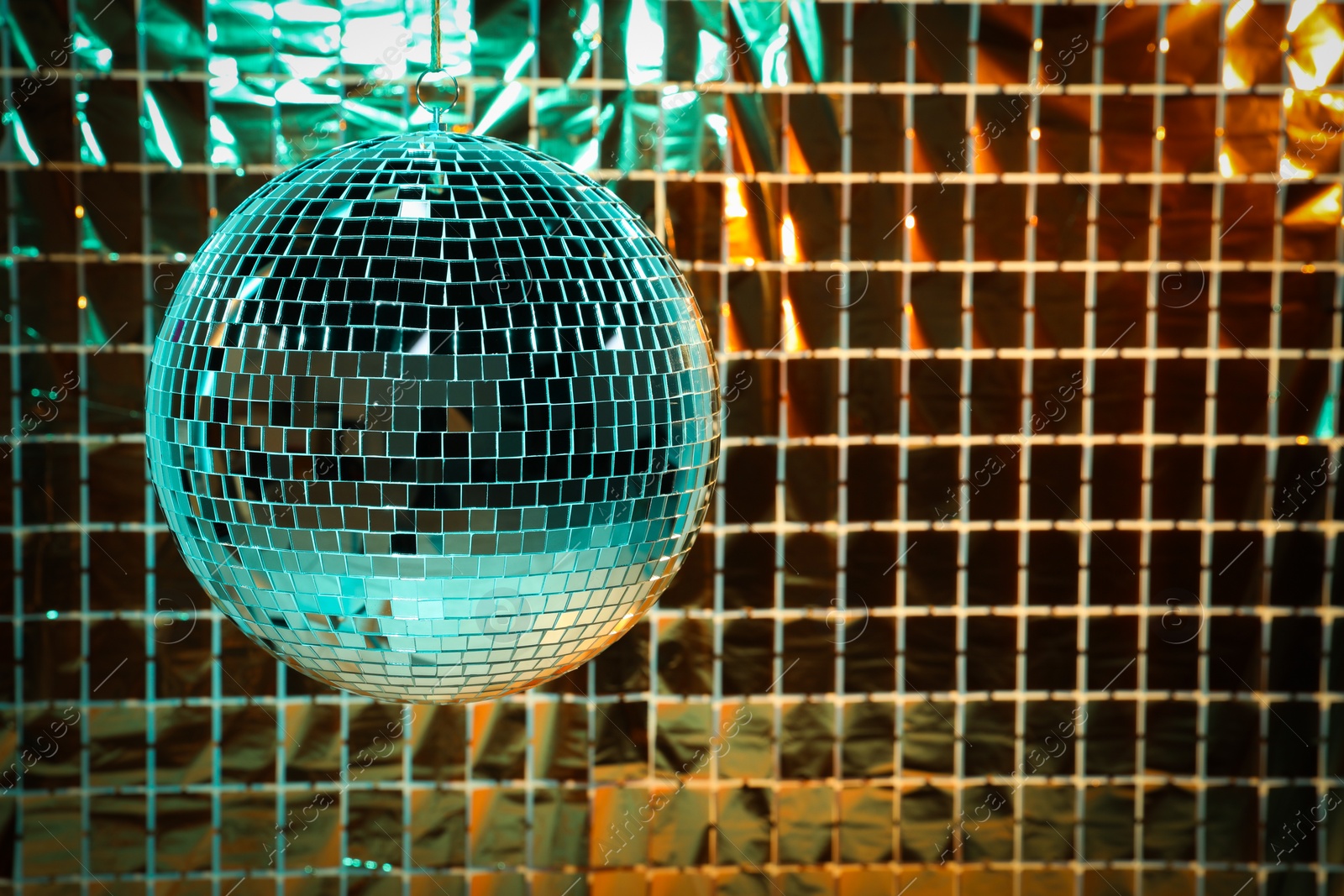 Photo of Shiny disco ball against foil party curtain under turquoise and orange light, space for text
