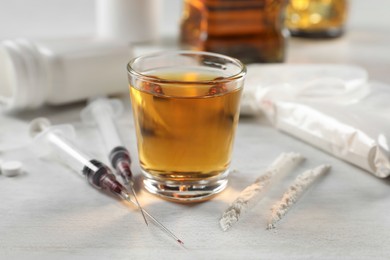 Photo of Alcohol and drug addiction. Whiskey in glass, syringes and cocaine on white table, closeup