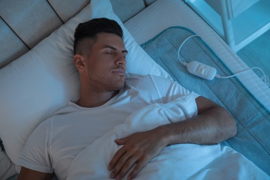 Man sleeping on electric heating pad in bed at night, above view