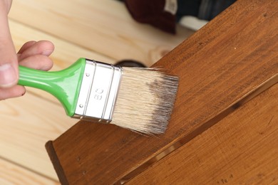 Photo of Man applying wood stain onto crate at table, closeup