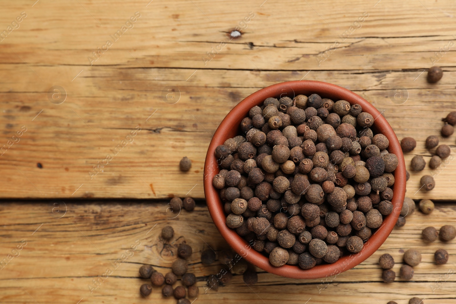 Photo of Aromatic allspice pepper grains in bowl on wooden table, top view. Space for text