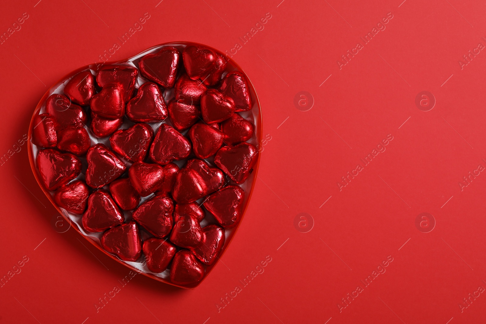 Photo of Tasty chocolate heart shaped candies in box on red background, top view. Space for text