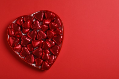 Photo of Tasty chocolate heart shaped candies in box on red background, top view. Space for text