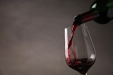 Photo of Pouring tasty red wine from bottle into glass on gray background, closeup. Space for text