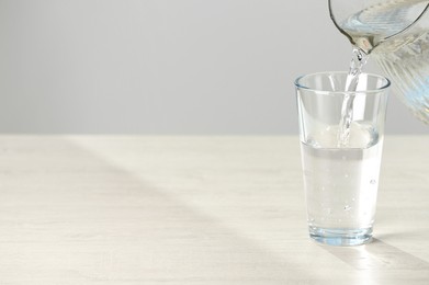 Photo of Pouring water from jug into glass on white table. Space for text