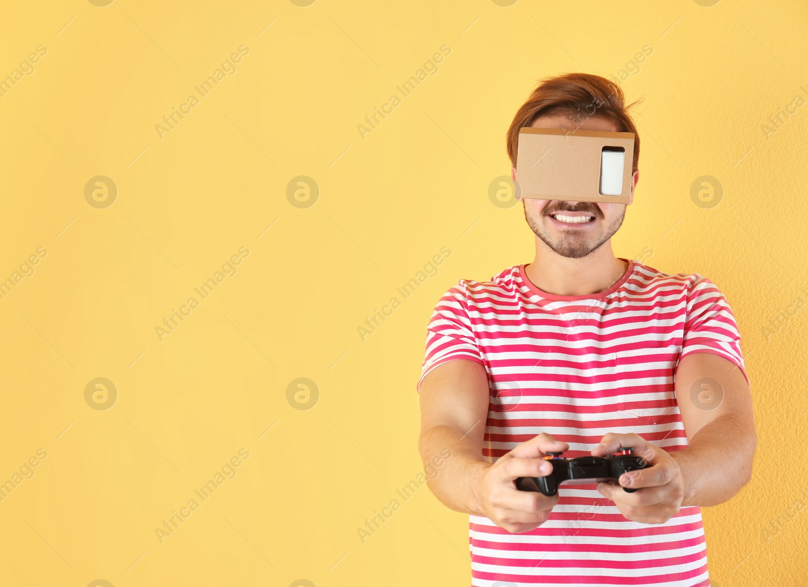 Photo of Young man using cardboard virtual reality headset on color background. Space for text