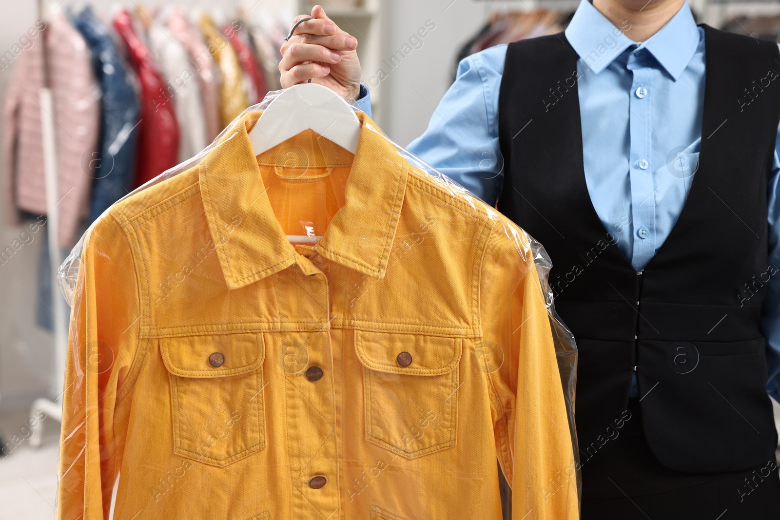 Photo of Dry-cleaning service. Woman holding shirt in plastic bag indoors, closeup