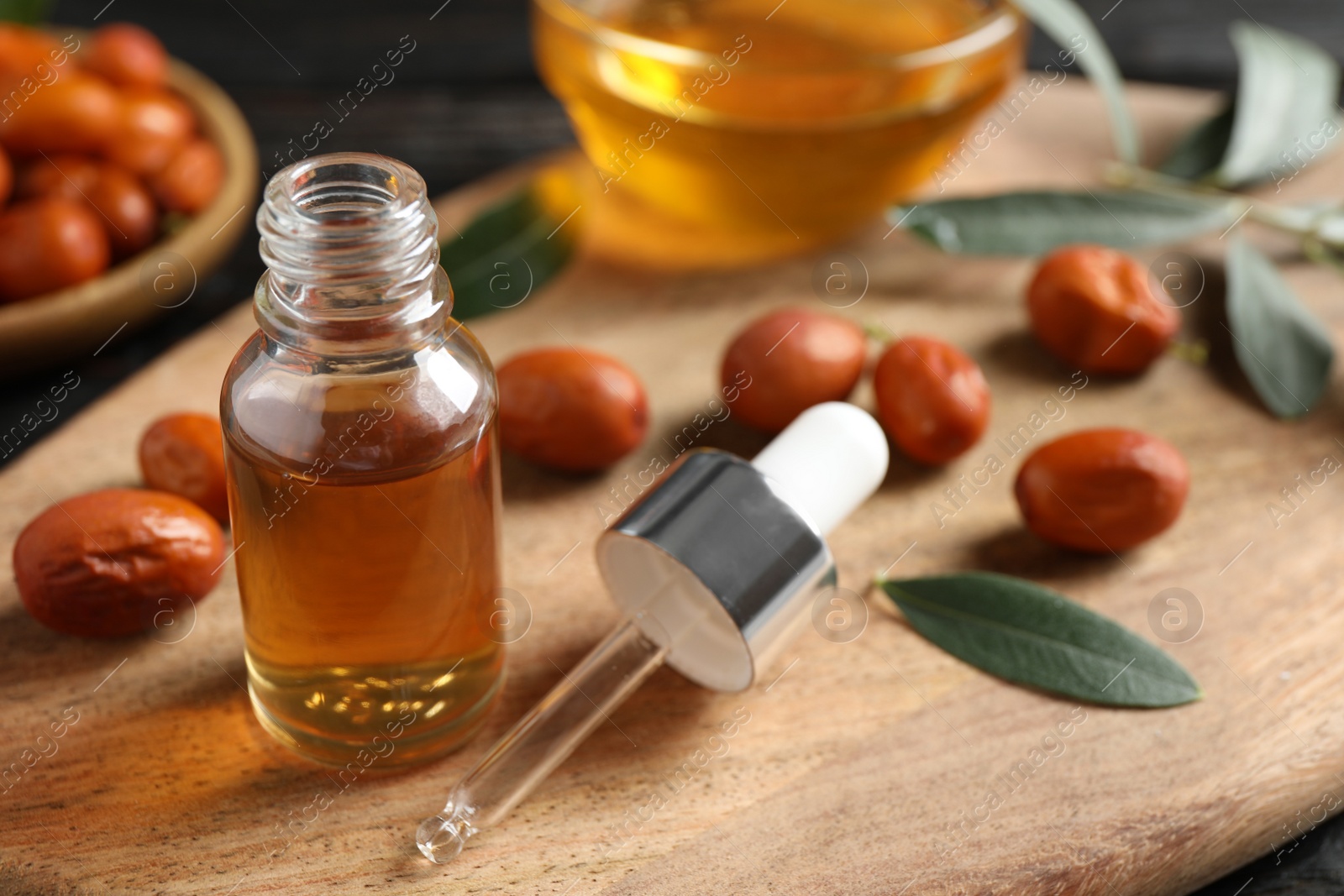 Photo of Glass bottle with jojoba oil and seeds on wooden board