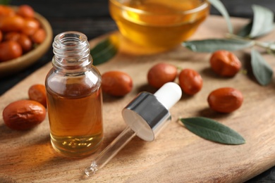 Photo of Glass bottle with jojoba oil and seeds on wooden board