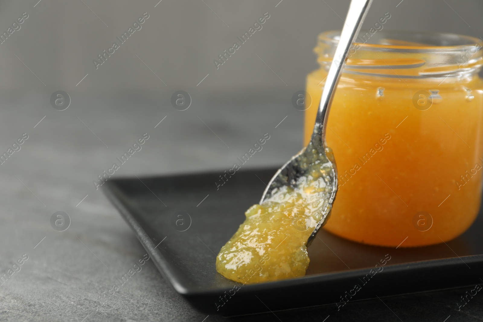 Photo of Delicious orange marmalade in jar and spoon on grey table, closeup. Space for text