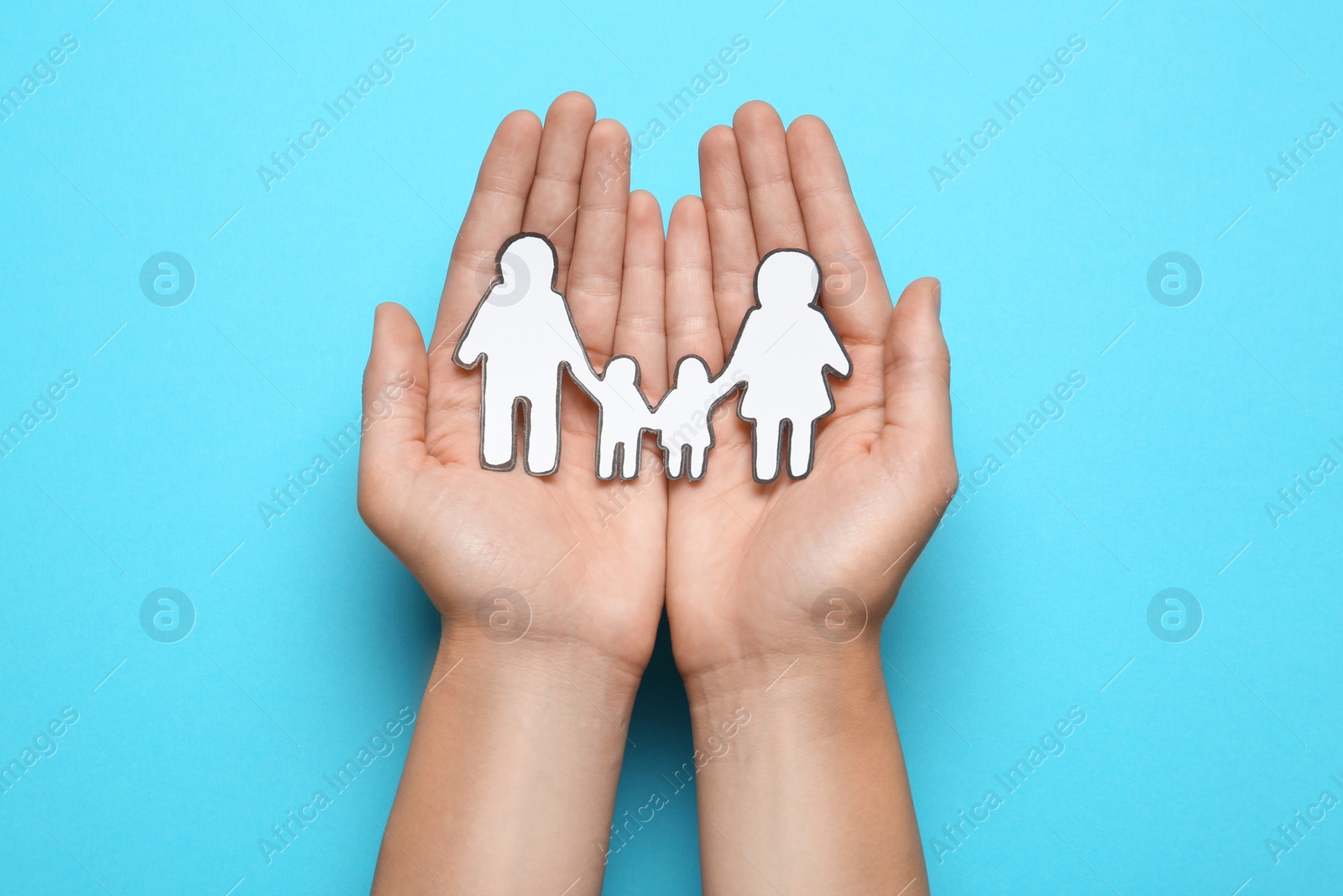 Photo of Woman holding paper family cutout on light blue background, top view