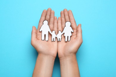 Woman holding paper family cutout on light blue background, top view